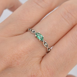 May include: A silver ring with a green marquise-shaped gemstone set in the center. The ring has a delicate, twisted band with small beads.