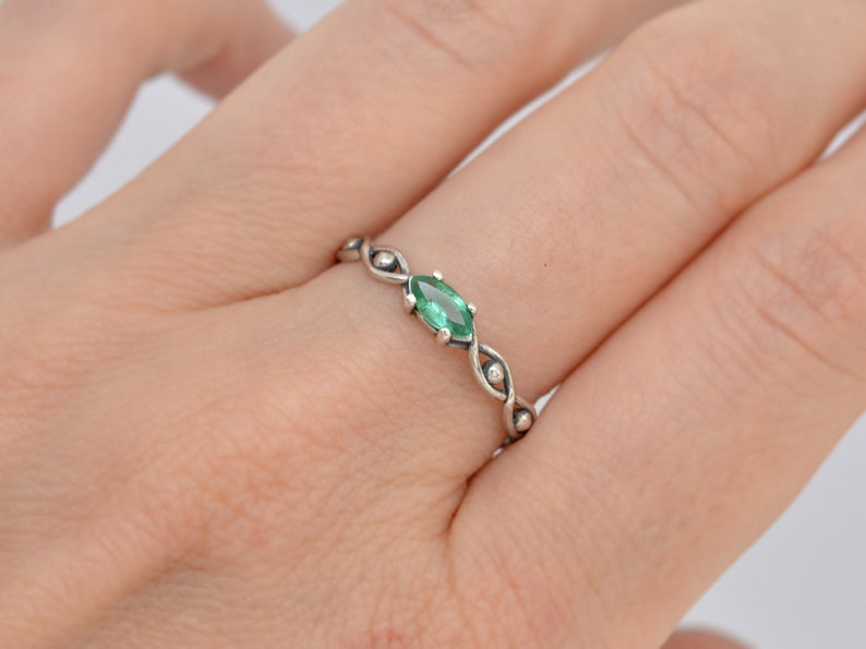 May include: A silver ring with a green marquise-shaped gemstone set in the center. The ring has a delicate, twisted band with small beads.