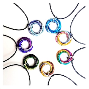 May include: A set of eight colorful, multi-layered metal rings on black cords. Each ring is a different color, including blue, purple, green, gold, and rainbow.