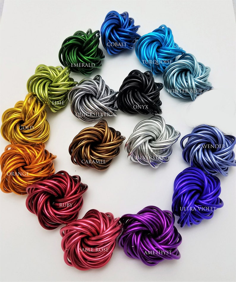 May include: A collection of 14 colorful metal fidget toys in various colors, including emerald green, cobalt blue, turquoise, winter blue, onyx black, quicksilver, gold, lavender, silverstar, caramel, orange, ruby, sable rose, and amethyst.