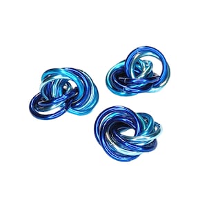 May include: Three blue and turquoise metal rings are intertwined to form a decorative knot. The rings are shiny and have a metallic finish.