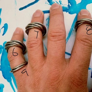 May include: A hand wearing four silver rings, each with a different number of bands. The rings are numbered 6, 7, 8, and 9.