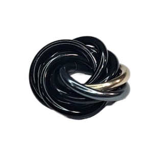 Puede incluir: Un anillo de nudo negro y dorado con un acabado liso y pulido. El anillo está hecho de múltiples bandas entrelazadas, creando un diseño complejo e intrincado.