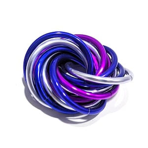 May include: A decorative metal knot sculpture composed of intertwined, curved tubes. The sculpture features a color palette of silver, deep blue, and vibrant purple. The object is set against a plain white background, highlighting its form and colors.