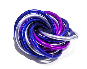 May include: A decorative metal knot sculpture composed of intertwined, curved tubes. The sculpture features a color palette of silver, deep blue, and vibrant purple. The object is set against a plain white background, highlighting its form and colors.