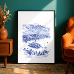 May include: A framed art print featuring a blue ink sketch of a lake with a small island church, surrounded by dense forests and tall mountain peaks in the background. The illustration includes technical architectural lines and ink splatters.