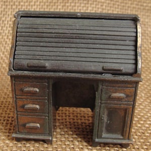May include: Miniature antique roll-top desk in a dark bronze finish. The desk features a slatted roll-top, three drawers on the left, and a cabinet with a drawer on the right. A charming decorative piece.