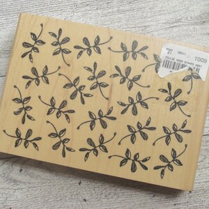 May include: A rectangular wooden stamp with a repeating pattern of black leaf sprigs. The stamp has a light brown color and a sticker with the number 1009 on it. The leaf design is a simple, hand-drawn style.