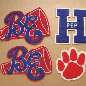 May include: A collection of embroidered patches in red, blue, and white. Includes two megaphone-shaped patches with "BE" in blue, a blue "H" patch with "PEP", and a red paw print patch. Ideal for varsity jackets or team apparel.