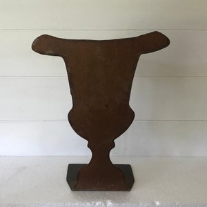 Peut inclure: Un vase en métal rouillé avec une base large et plate et un corps haut et mince. Le vase a la forme d'une urne traditionnelle avec un sommet arrondi et une poignée décorative.