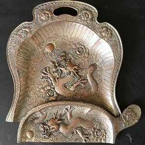 Peut inclure: Un plateau de service en argent avec un motif orné représentant deux dragons. Le plateau a un bord festonné et une poignée sur le dessus.
