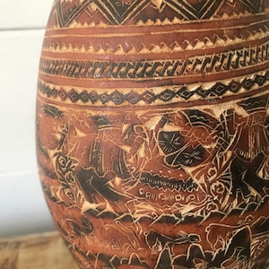 May include: A brown gourd with intricate carvings of people and animals. The gourd is decorated with geometric patterns in black and brown.
