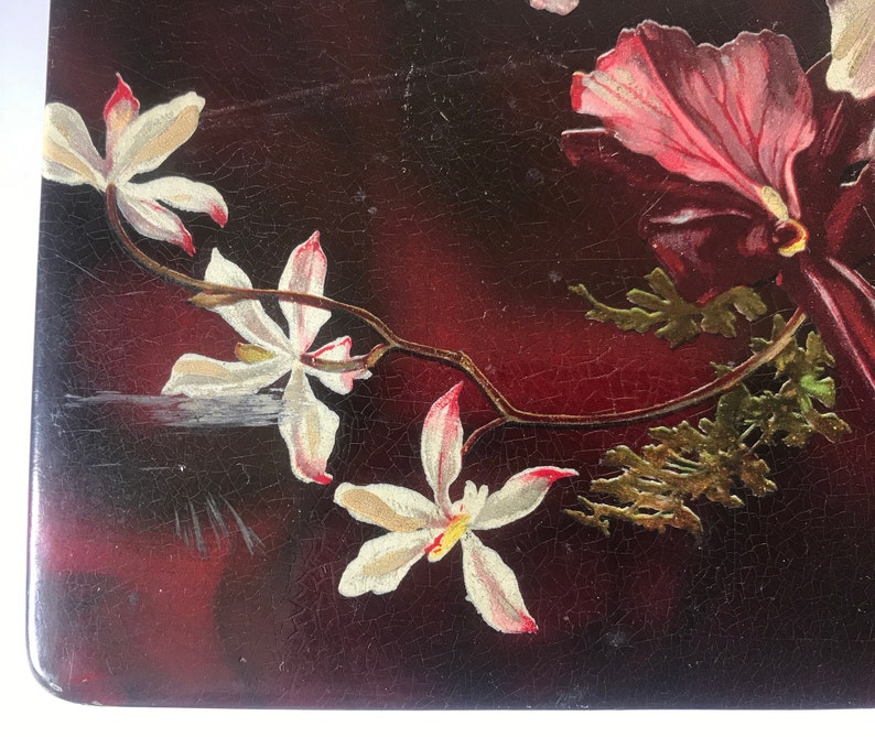 May include: A close-up of a dark red background with a white flower and a pink flower. The flowers are painted on the surface and have a vintage look.