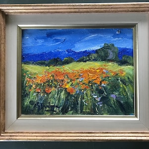 Puede incluir: Una pintura al óleo enmarcada que representa un campo de flores silvestres naranjas en primer plano con un cielo azul y montañas distantes en el fondo.