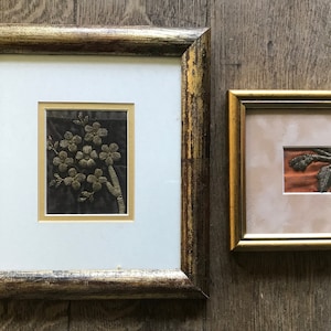 Peut inclure: Deux pièces de broderie encadrées, l'une avec un motif floral en fil d'or sur fond noir, et l'autre avec un motif feuillu en fil brun sur fond orange.