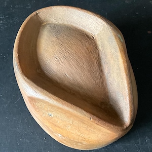May include: A handcrafted wooden bowl with a natural, light brown finish. The bowl has an elongated, oval shape with gently curved sides and a smooth interior. The wood grain is visible, adding to its rustic charm. The bowl is empty.