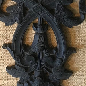 May include: A black, ornate, decorative wall hanging with a floral design. The design is intricate and detailed, with a central point and flowing lines.