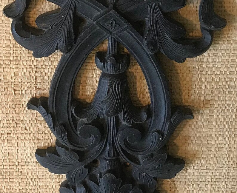 May include: A black, ornate, decorative wall hanging with a floral design. The design is intricate and detailed, with a central point and flowing lines.