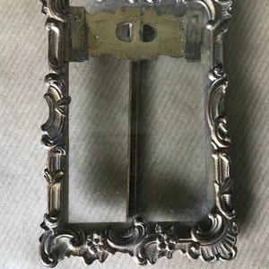 May include: A vintage ornate gold-toned metal picture frame with a glass pane. The frame has a decorative design with floral motifs and scrolls.