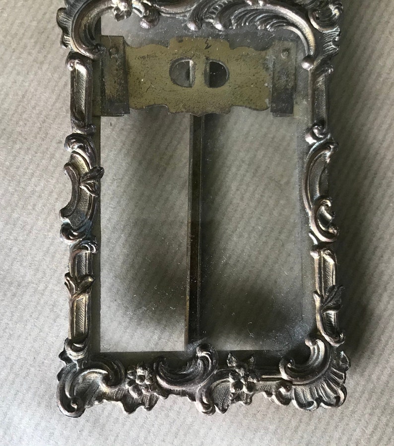 May include: A vintage ornate gold-toned metal picture frame with a glass pane. The frame has a decorative design with floral motifs and scrolls.