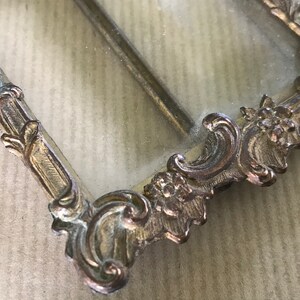 May include: A vintage ornate silver picture frame with a glass insert. The frame has a detailed design with floral motifs.