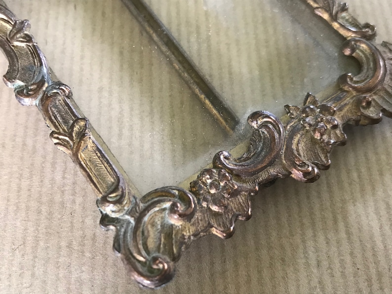 May include: A vintage ornate silver picture frame with a glass insert. The frame has a detailed design with floral motifs.