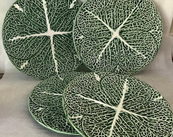 Puede incluir: Cuatro platos de ensalada de cerámica verde y blanca con un diseño de hoja de col. Los platos están apilados uno encima del otro.