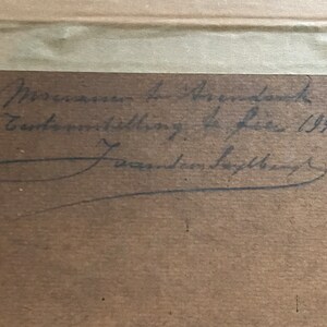 May include: A close-up of a brown paper with black ink handwriting. The text reads "Museum in Amsterdam, Tentoonstelling de Luxe 1941,  J. van den Bergh".