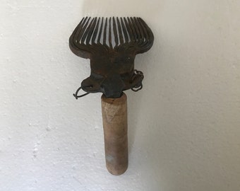 Könnte beinhalten: Ein antiker Wollkamm aus Metall mit einem Holzgriff. Der Kamm hat eine rostige Oberfläche und ist zum Kämmen von Wolle gedacht.