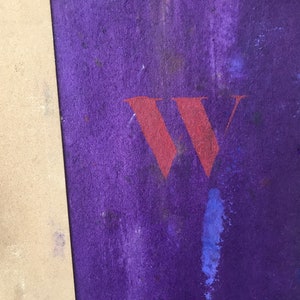 May include: A close-up of a purple surface with a large red "W" painted on it. The surface is textured and has a few spots of blue paint.