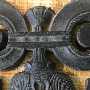 May include: A black wooden decorative piece with intricate carvings in the shape of a heart. The piece has a central design with a floral motif and two symmetrical scrolls on either side.