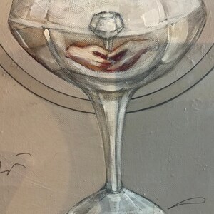 May include: A clear glass goblet with a thick stem and a wide bowl. The bowl is filled with a clear liquid and a small, clear crystal is suspended in the centre. The crystal is casting a shadow on the bottom of the bowl.