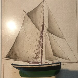May include: A watercolour painting of a sailboat with brown sails and a green hull. The sailboat is framed and ready to hang.