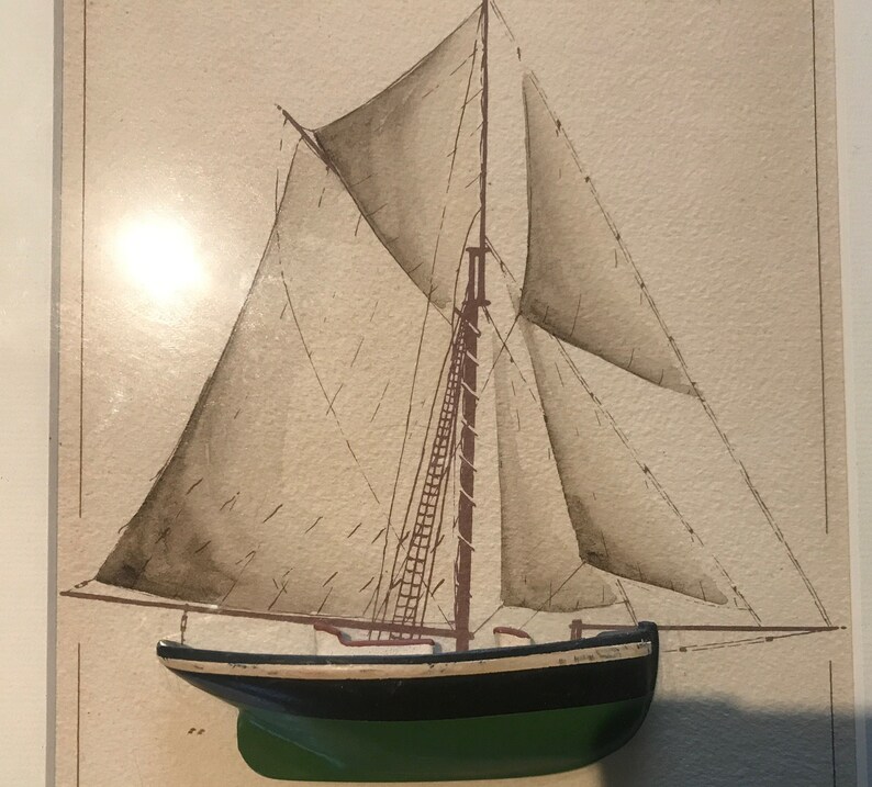May include: A watercolour painting of a sailboat with brown sails and a green hull. The sailboat is framed and ready to hang.