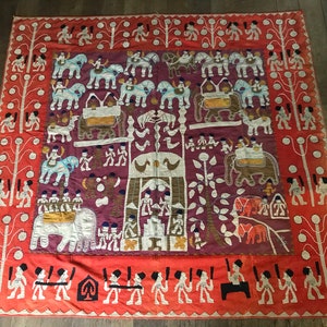 May include: A colorful hand-stitched textile wall hanging with a central design of a tree and animals. The background is a deep purple with white and orange accents. The border is a bright orange with white figures.