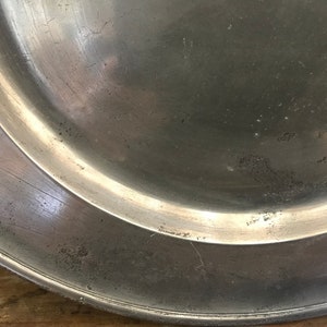 May include: A silver-colored metal plate with a slightly raised rim. The plate has a smooth, shiny surface with some scratches and marks.