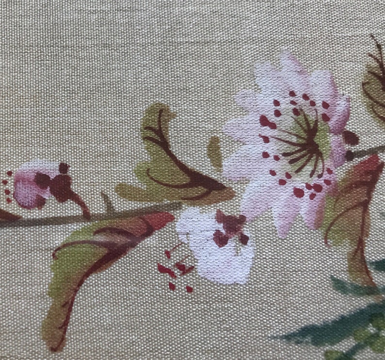 May include: A beige fabric with a floral design featuring pink and white flowers with brown stems and leaves.