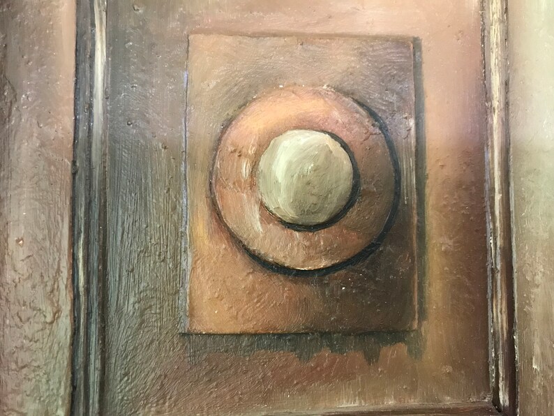 Op de afbeelding: Een close-up van een houten deur met een geschilderd detail van een cirkel in een vierkant. De cirkel is bruin met een kleinere, cr&egrave;mekleurige cirkel in het midden.
