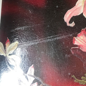 May include: Close-up of a vintage postcard with a floral design. The postcard features pink and white flowers on a dark background with a textured surface.