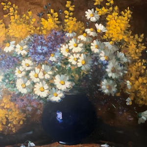 May include: A blue ceramic vase filled with a bouquet of white daisies and yellow wildflowers. The flowers are arranged in a loose, natural style, and the vase is sitting on a wooden table.