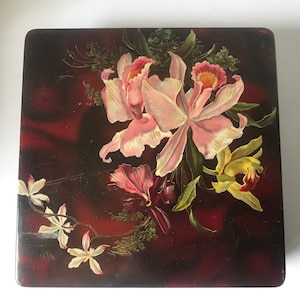 May include: A vintage wooden box with a floral design. The box features a painted image of pink and yellow orchids on a dark red background.