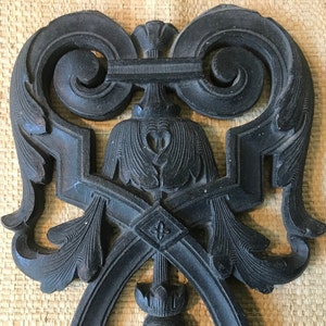 May include: A black metal decorative wall hanging with intricate floral and scroll designs. The design is symmetrical and features a central heart shape.