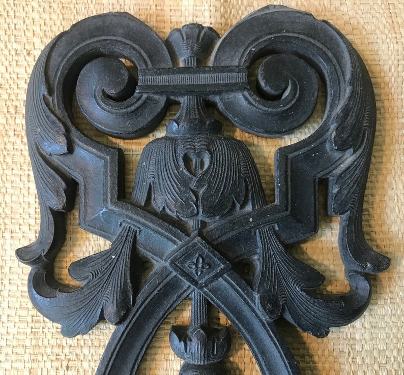 May include: A black metal decorative wall hanging with intricate floral and scroll designs. The design is symmetrical and features a central heart shape.