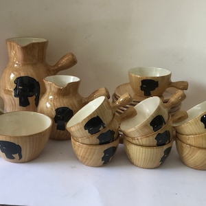 Op de afbeelding: Een set van keramische koffiekopjes met een houten look en een bijpassende roomkan en kan. De kopjes hebben zwarte silhouetten van mensen.