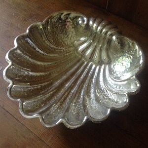 May include: A silver-colored, decorative, shell-shaped dish. The dish has a textured, hammered finish.