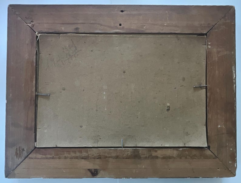 May include: Back of a framed painting. The wooden frame is a medium brown color with visible wood grain. The backing is a light tan color, secured with metal staples and a single nail.