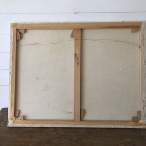 Op de afbeelding: De achterkant van een gespannen canvas schilderij met een houten lijst. Het canvas is wit en de lijst is van natuurlijk hout. De achterkant van de lijst heeft een houten steun met het nummer "52x45" erop.