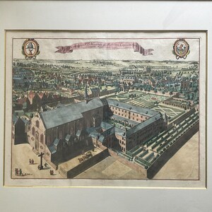 May include: An antique, framed, hand-colored print depicting a detailed aerial view of a European town with buildings, gardens, and a church. The print includes text on a banner and decorative elements.