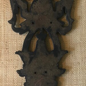 May include: A dark brown wooden wall decor with intricate carvings in the shape of a stylized floral design. The decor has two holes at the top for hanging.