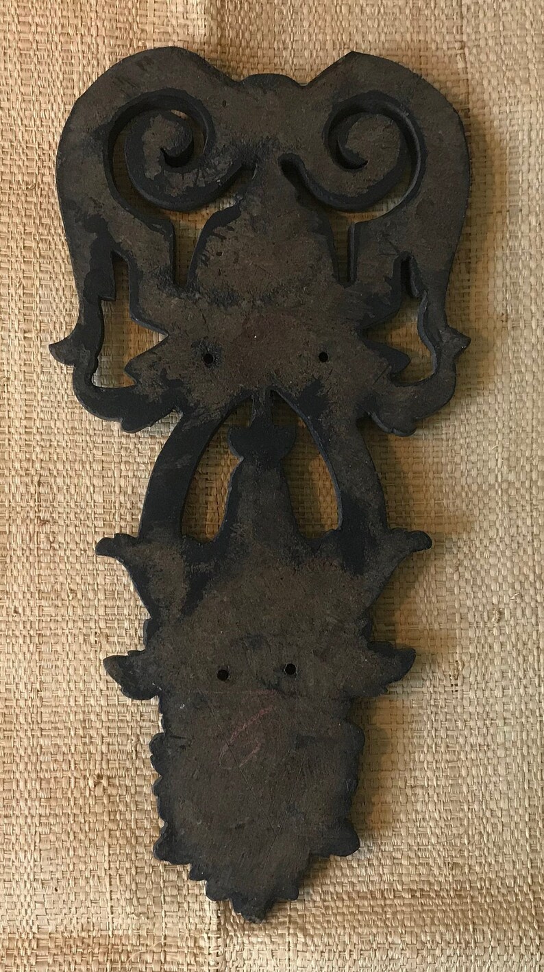 May include: A dark brown wooden wall decor with intricate carvings in the shape of a stylized floral design. The decor has two holes at the top for hanging.